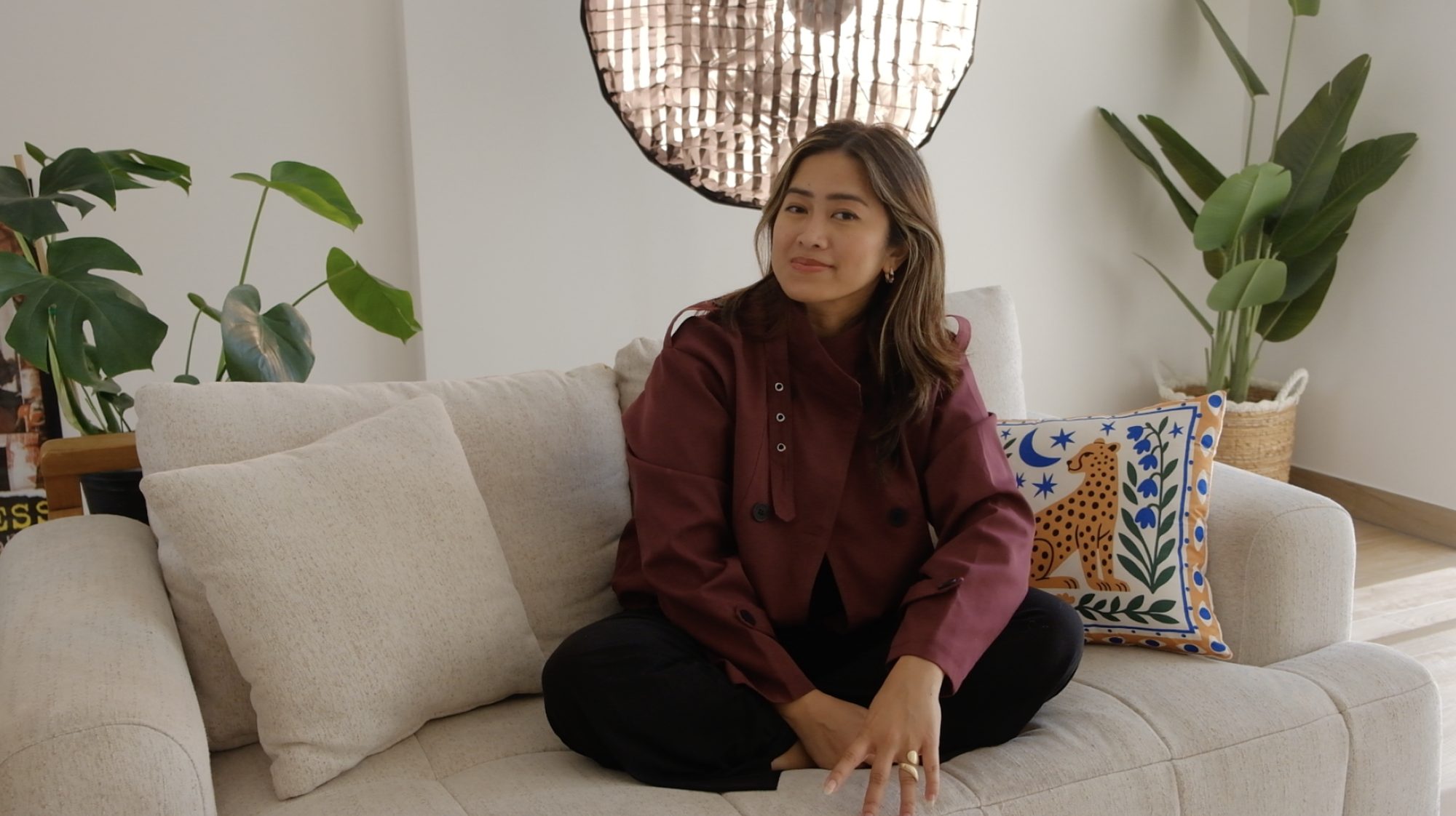 Jewels Mercado, founder of Content Club HQ, sitting cross-legged on a cream sofa in the studio in Dubai