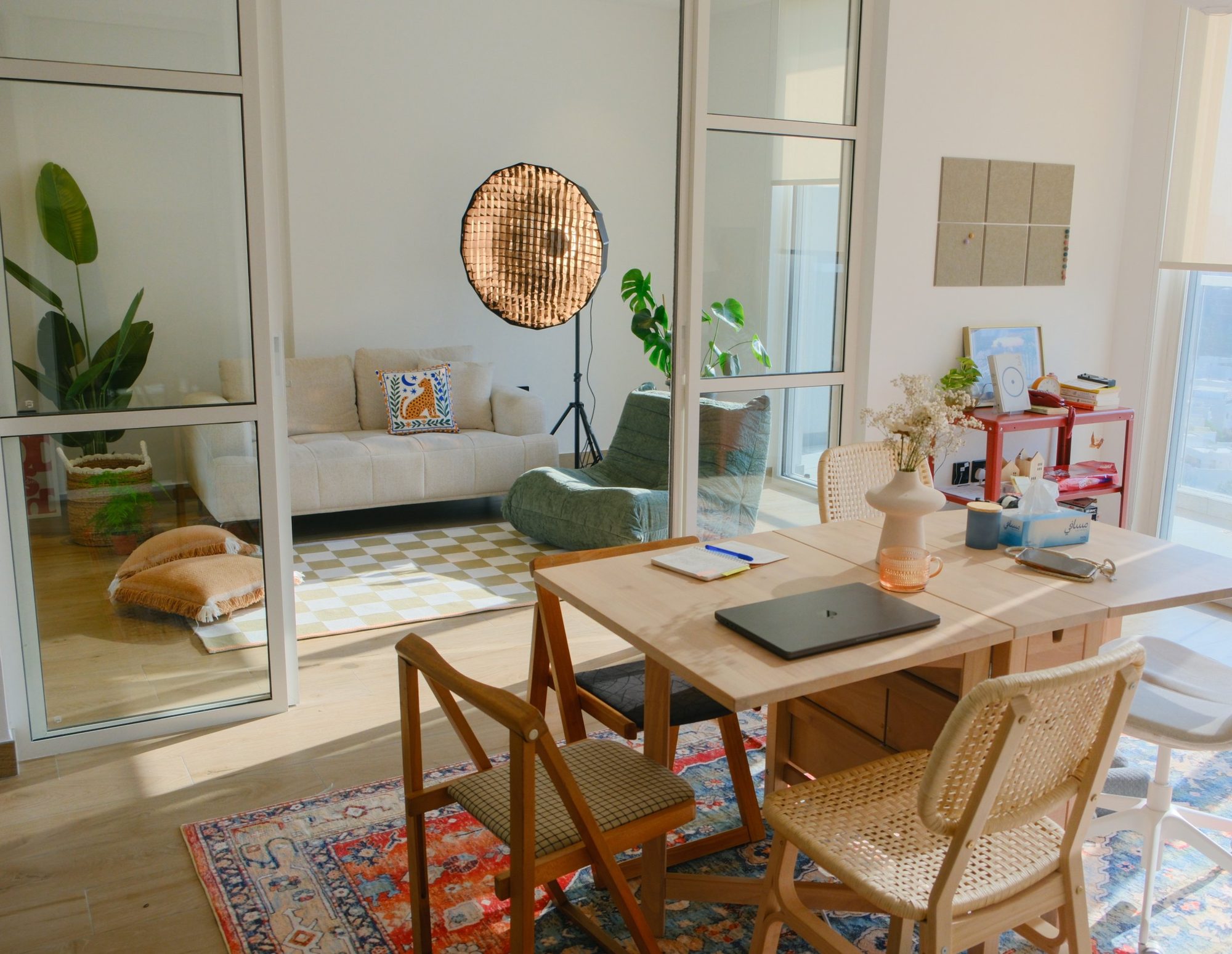 The Content Club HQ space: a sunlit wooden coworking table in front of a glass-walled studio with a cream sofa and a softbox light
