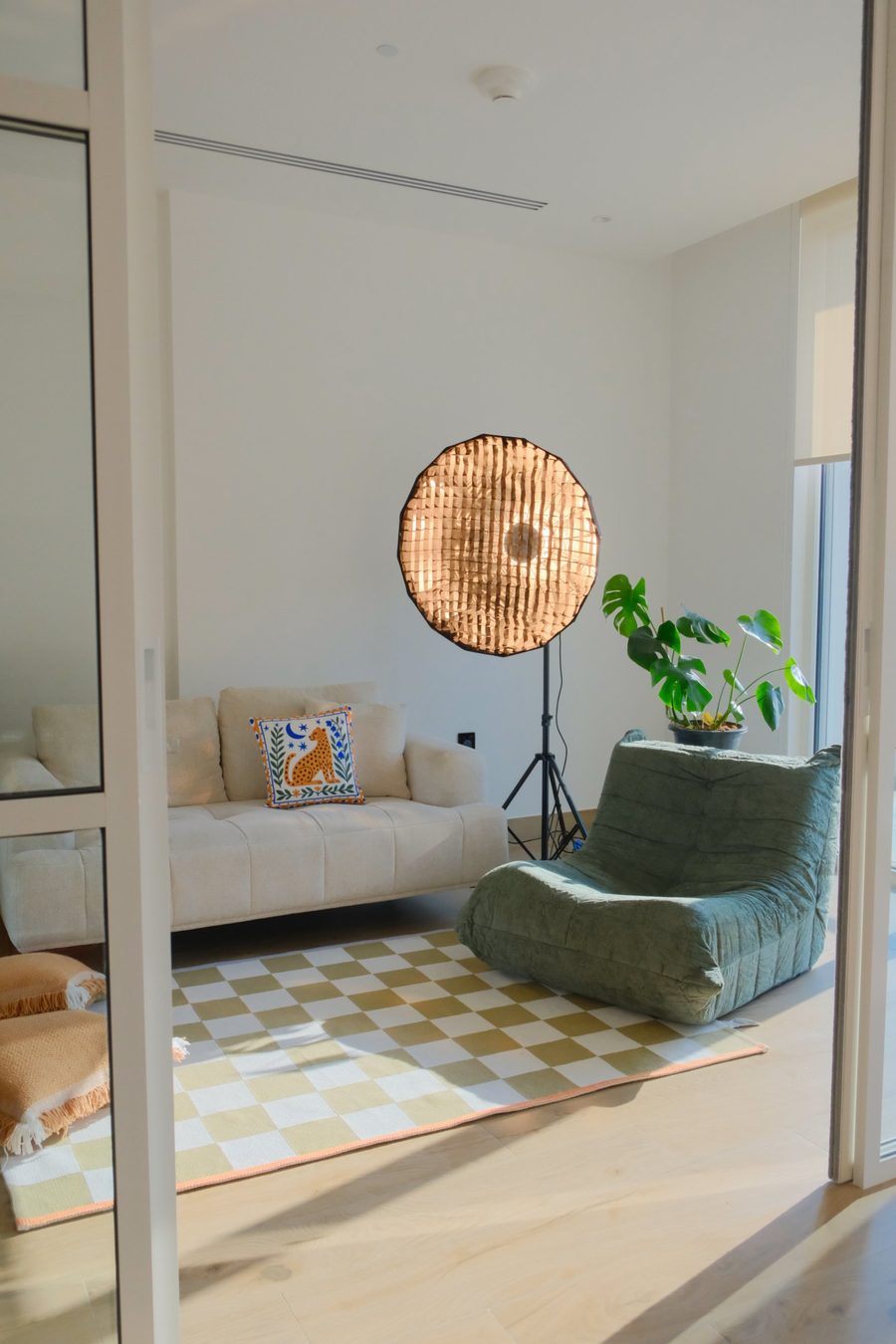 The studio corner with a cream sofa, a green lounge chair, a softbox light and a monstera plant