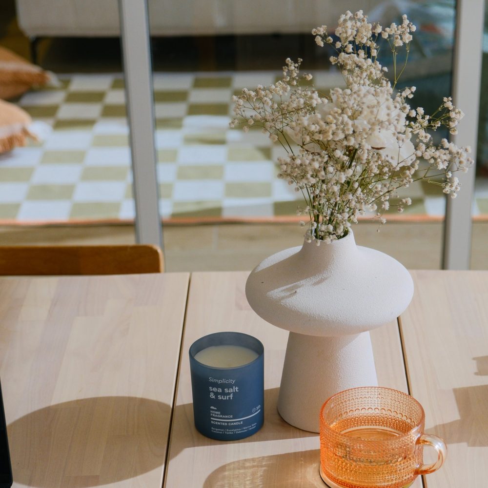Dried flowers in a vase, a candle and an amber glass cup on a sunlit wooden table