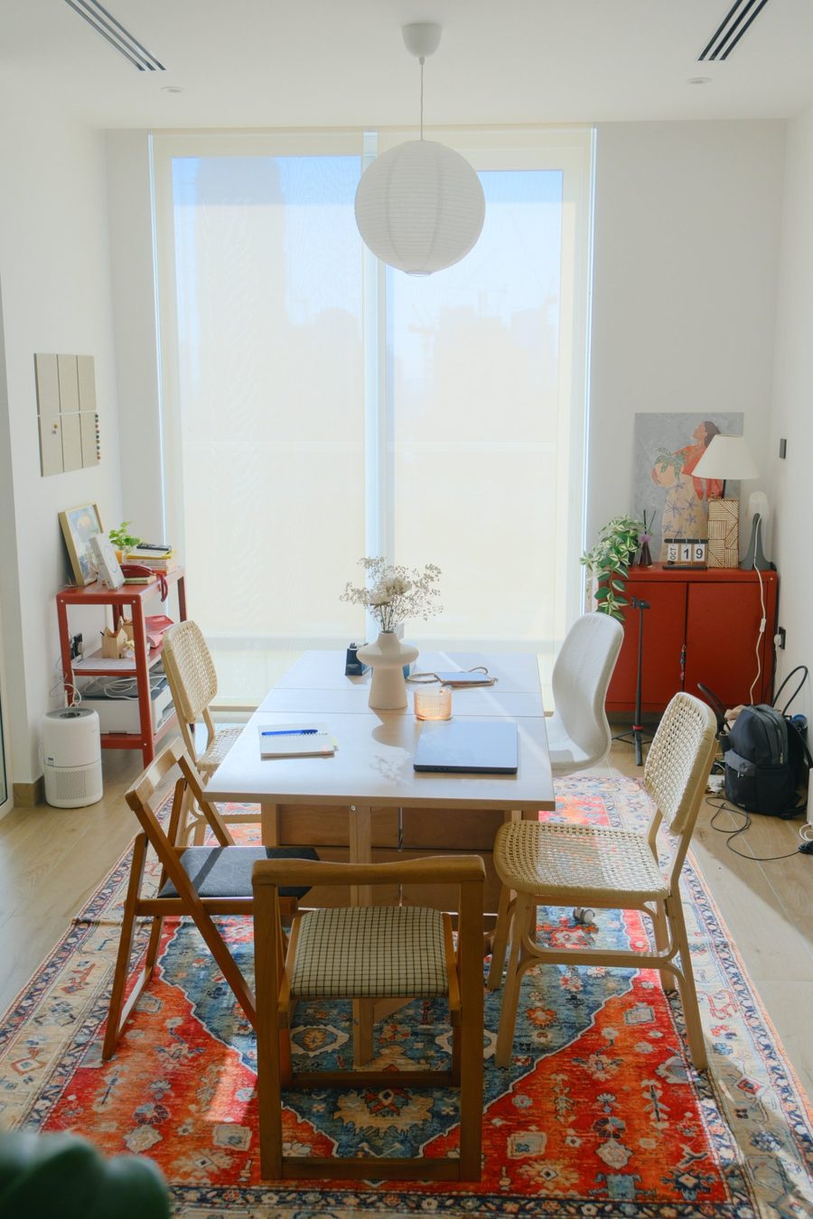 The coworking table by a large window, with rattan chairs, a paper lantern and a colorful rug